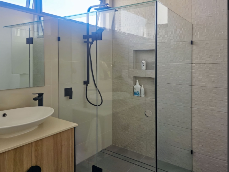 Modern bathroom with frameless glass enclosure and black fittings, showing a clear example of the cost to replace shower screen.